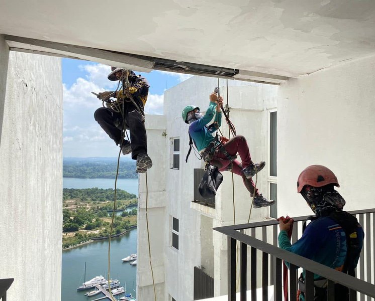 Rope-access technicians working on a high-rise façade above a marina